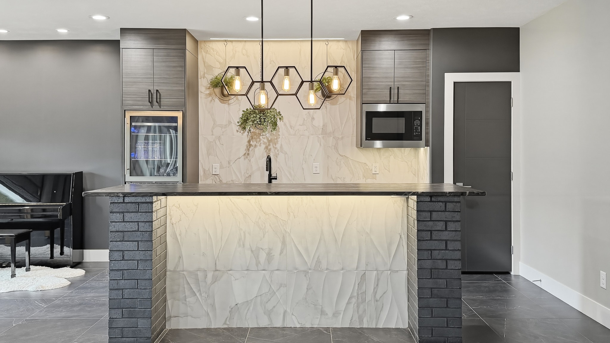Bar island with hexagon pendant lights, marble tile backsplash and brick columns