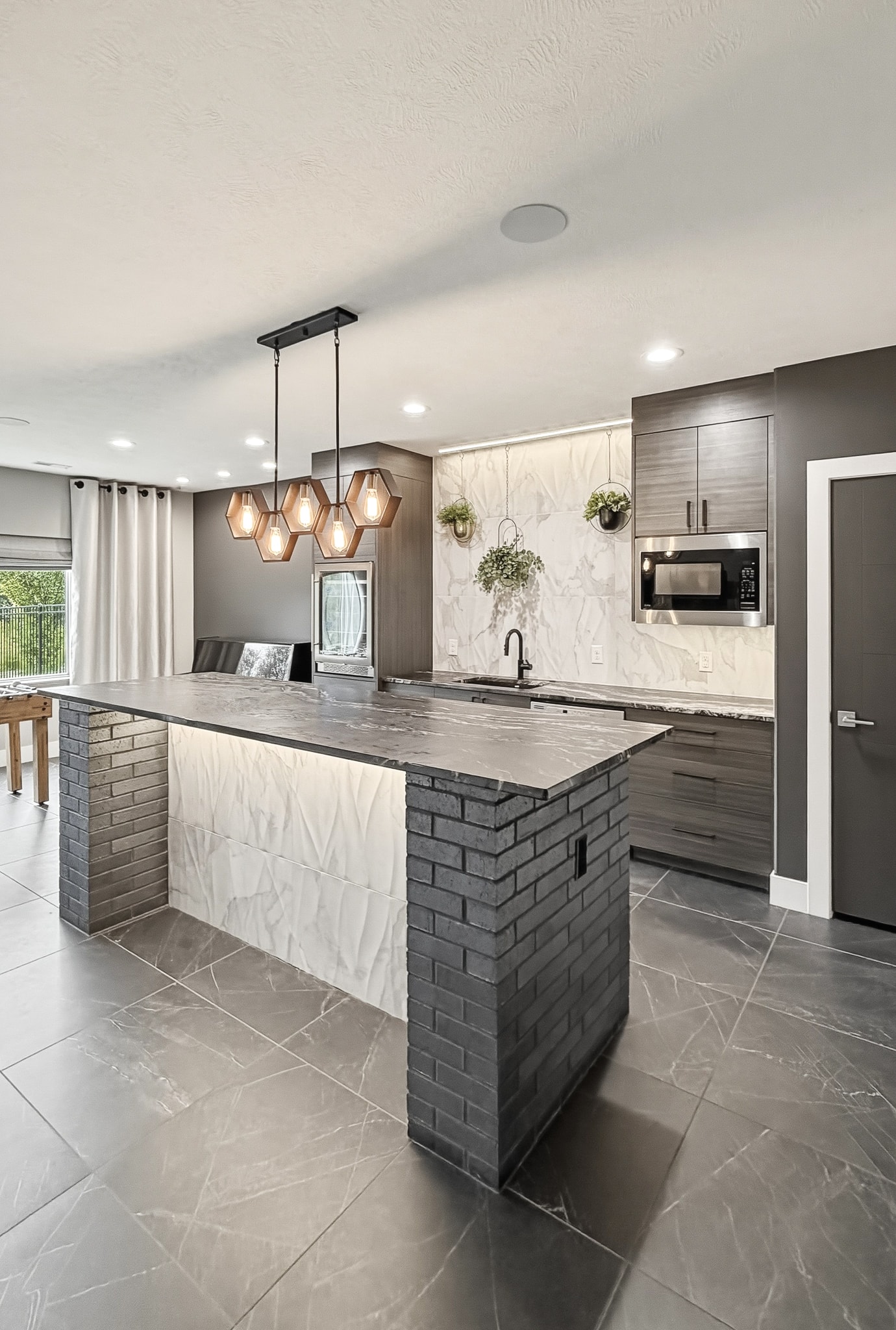 Wide view of bar with hexagon pendants, marble tile backsplash and dark tile floor
