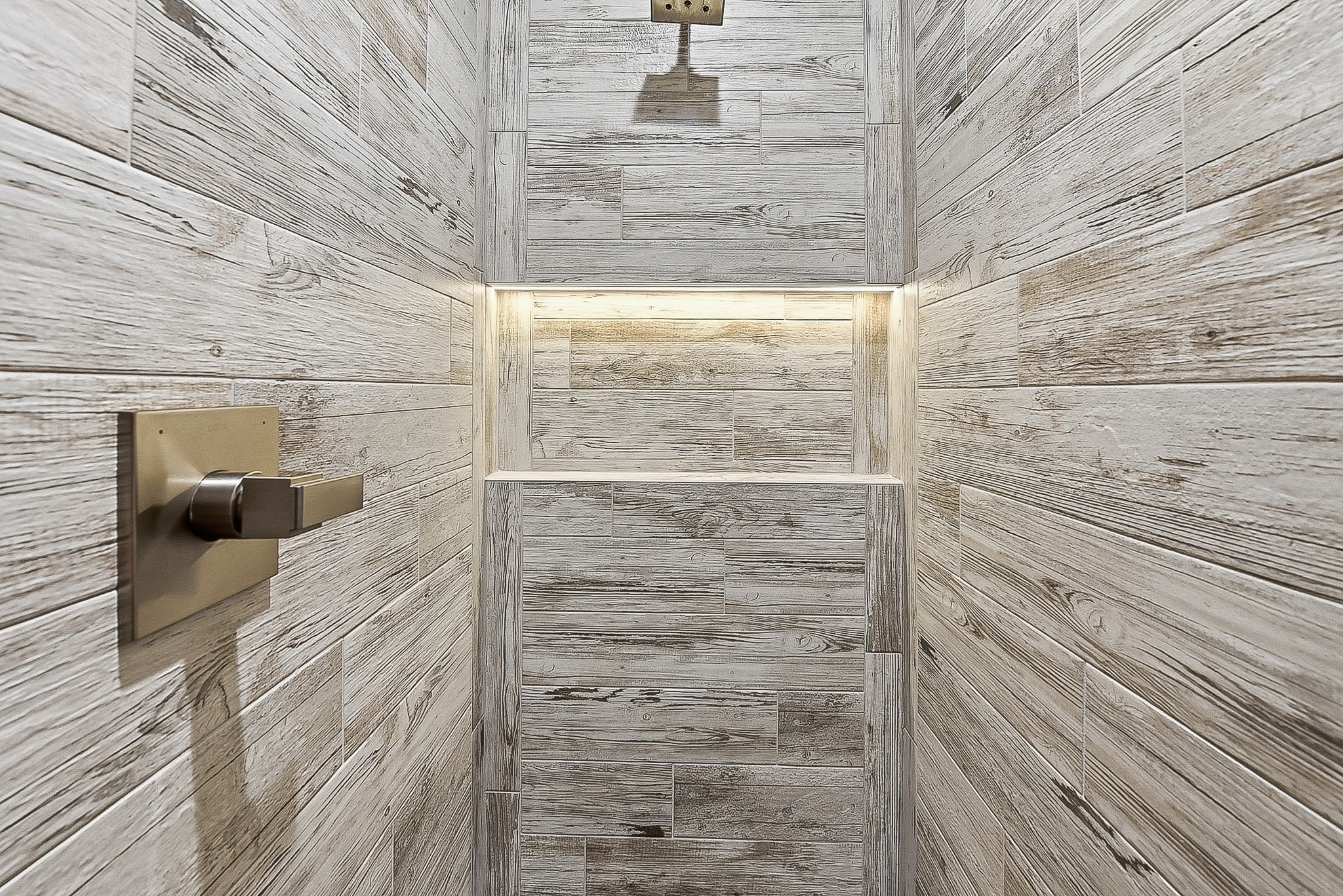Wood-look tile shower interior with illuminated niche and rain head