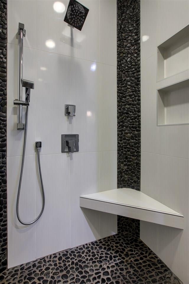 White subway tile shower with black pebble tile accents and corner bench