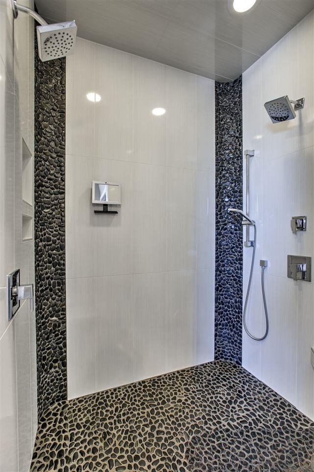 Walk-in shower with white tile and black pebble tile accents and dual showerheads