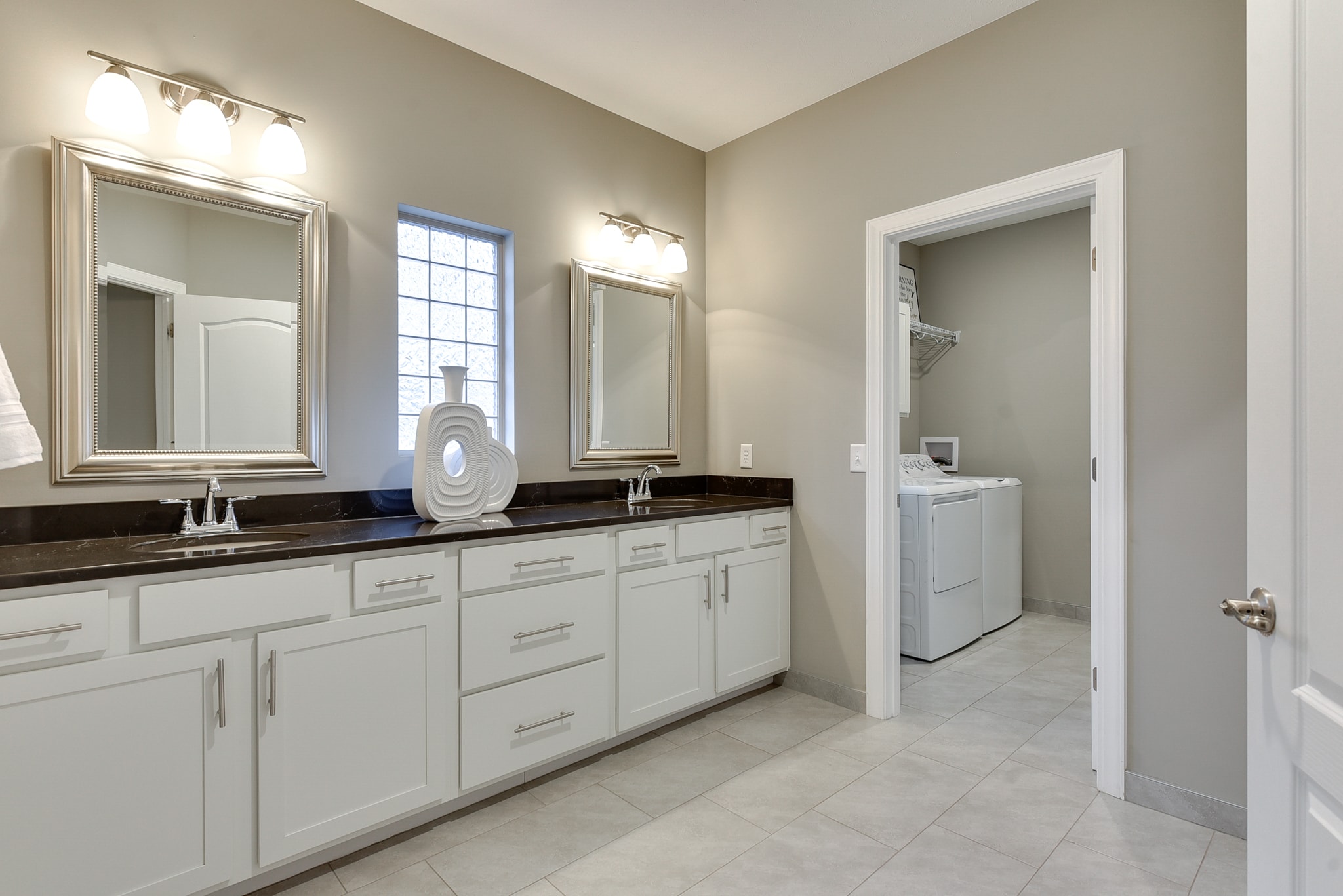 Double vanity with white cabinetry, dark granite countertop and large tile floor