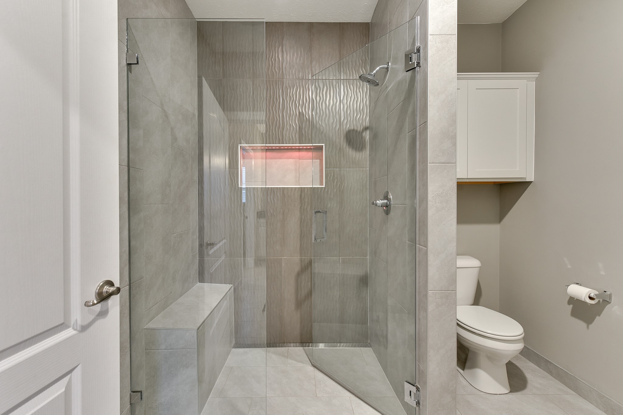 Glass enclosed shower with gray wave tile, illuminated niche and bench seat