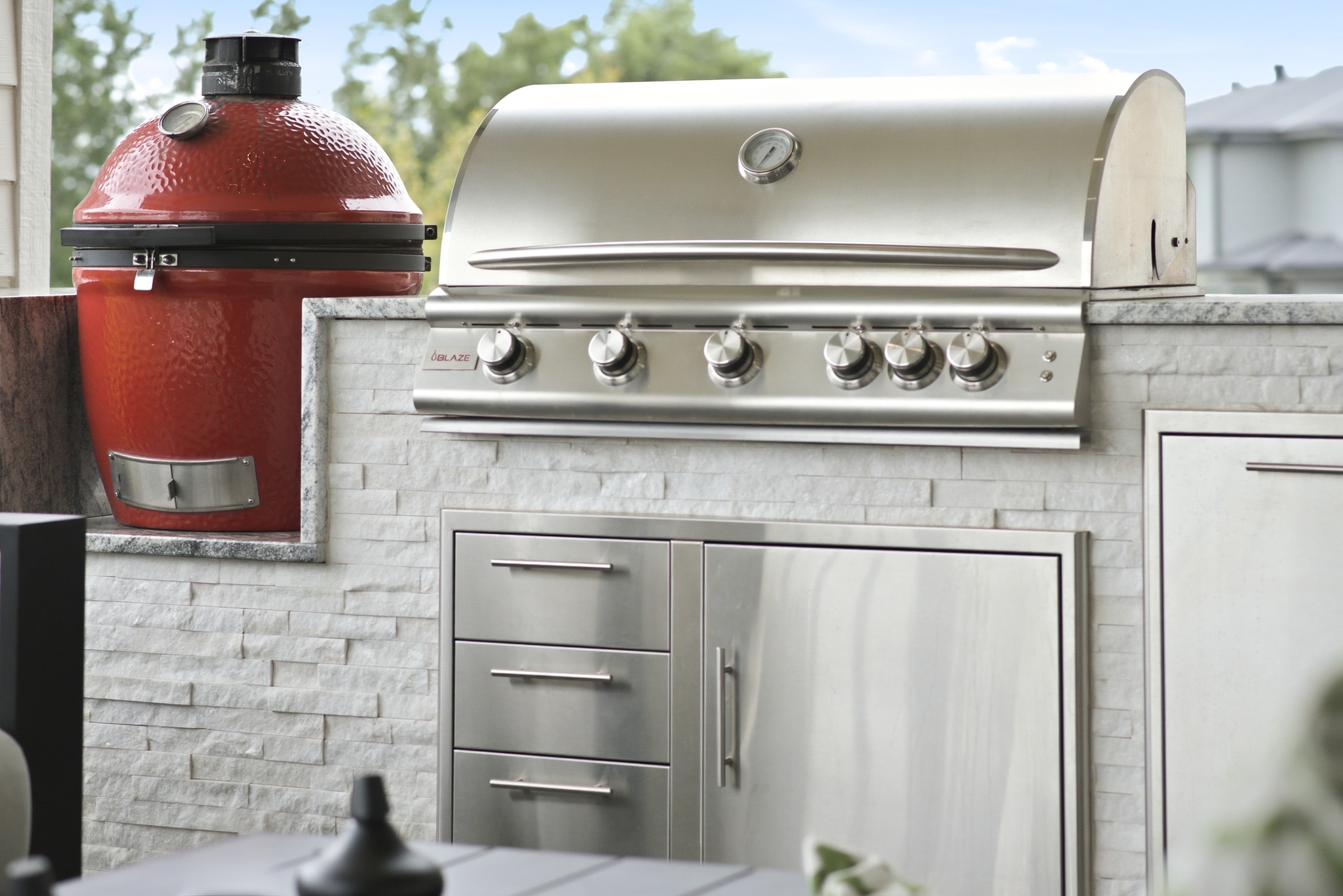 Outdoor kitchen with red ceramic grill, stainless gas grill and white stone tile surround