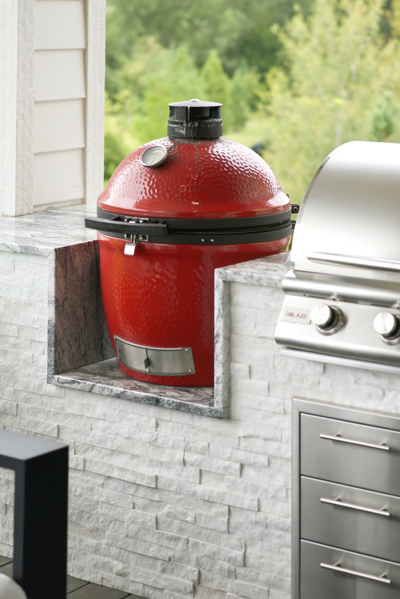 Close-up of red ceramic grill set into white stone tile outdoor kitchen island