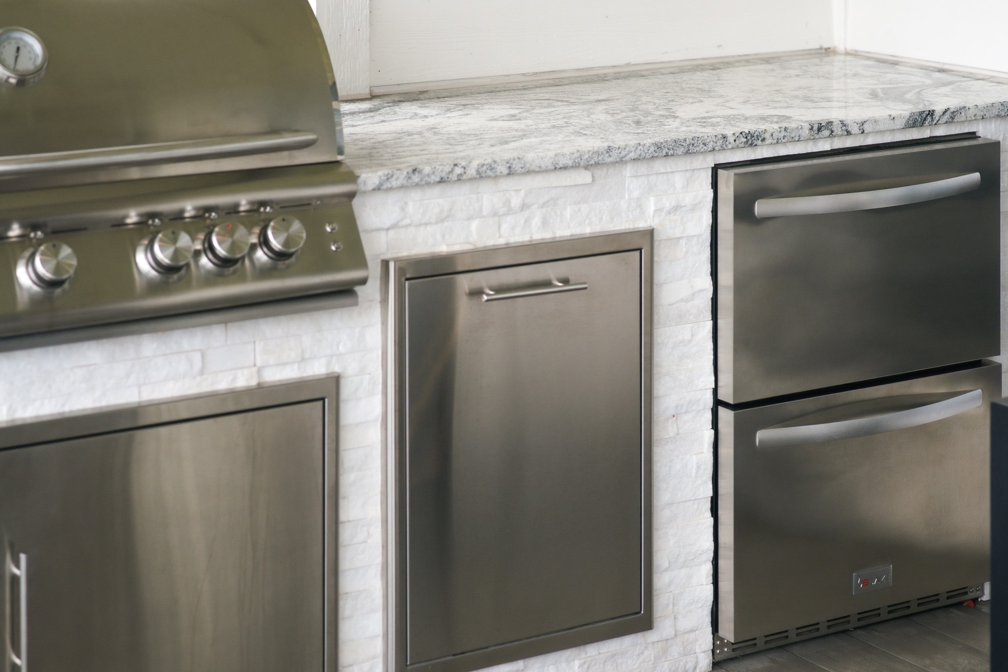 Outdoor kitchen with stainless appliances, white stone tile surround and granite countertop
