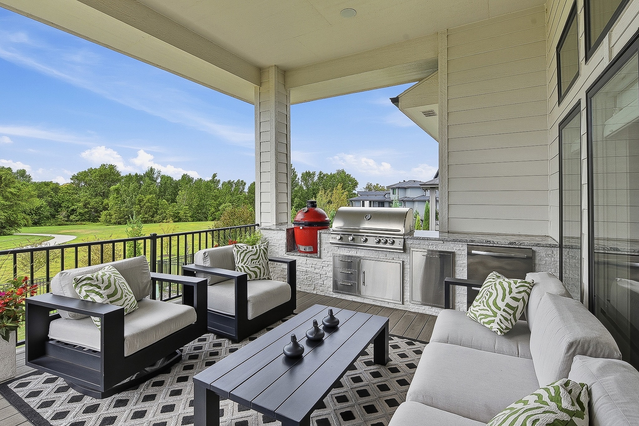 Covered deck with outdoor kitchen, red grill, lounge seating and open backyard views