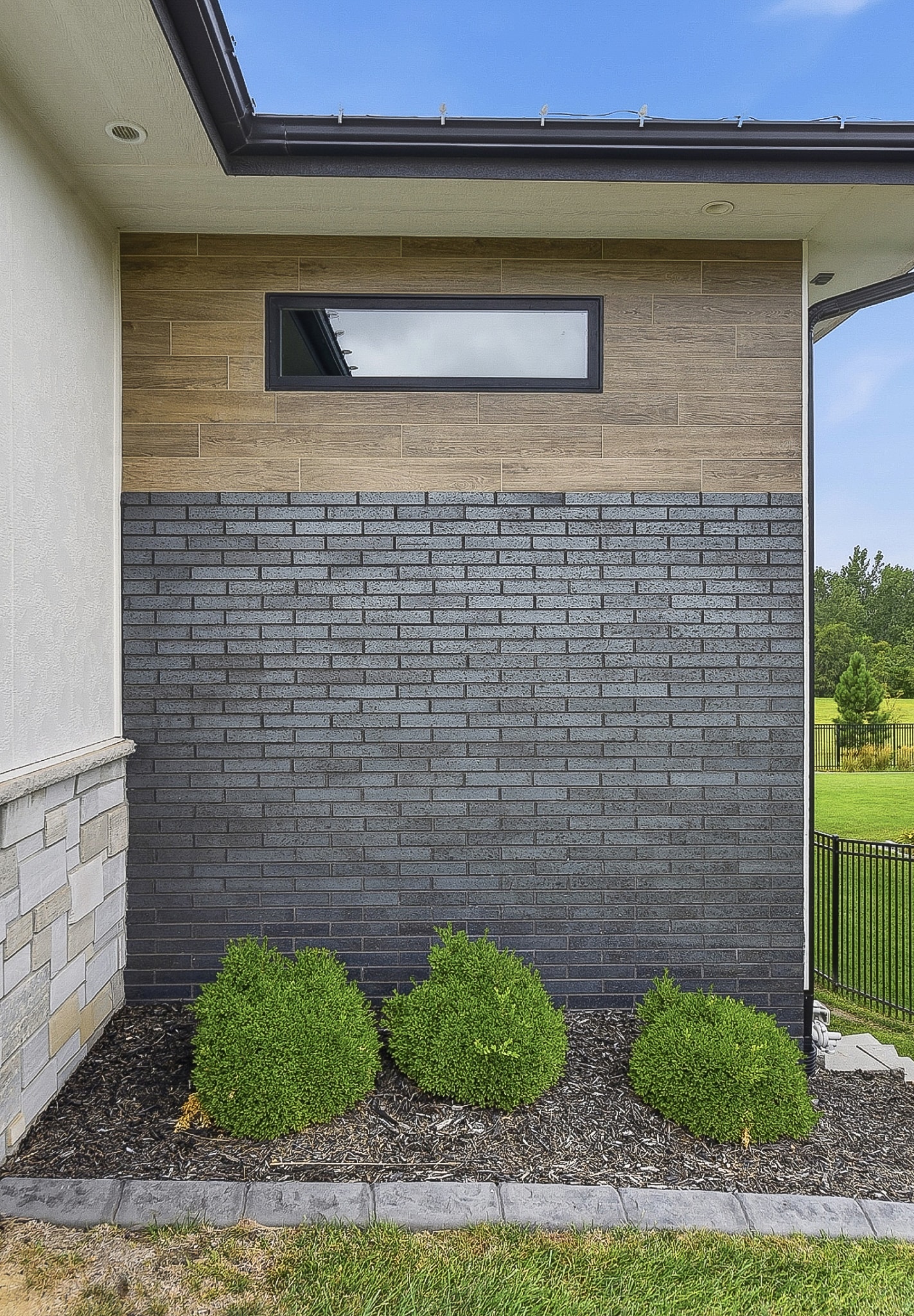 House exterior with black brick-look tile cladding, wood-grain tile accent band and landscaping