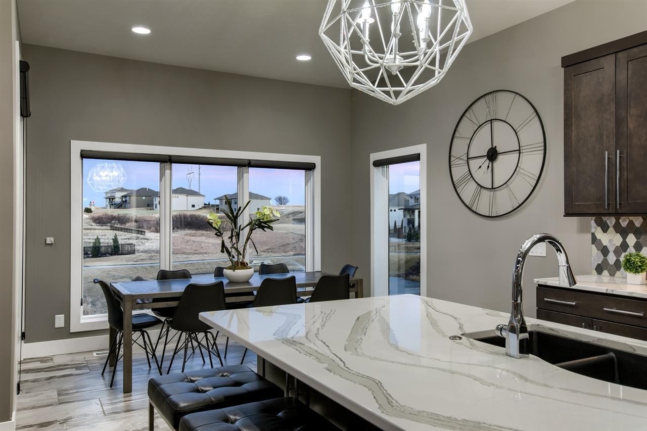 Kitchen and dining area with marble island, geometric chandelier and large windows overlooking neighborhood