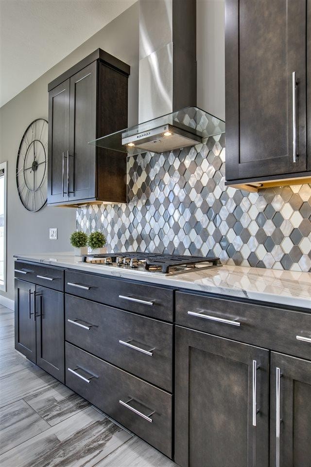 Close-up of diamond tile backsplash behind gas cooktop with dark cabinetry and stainless range hood