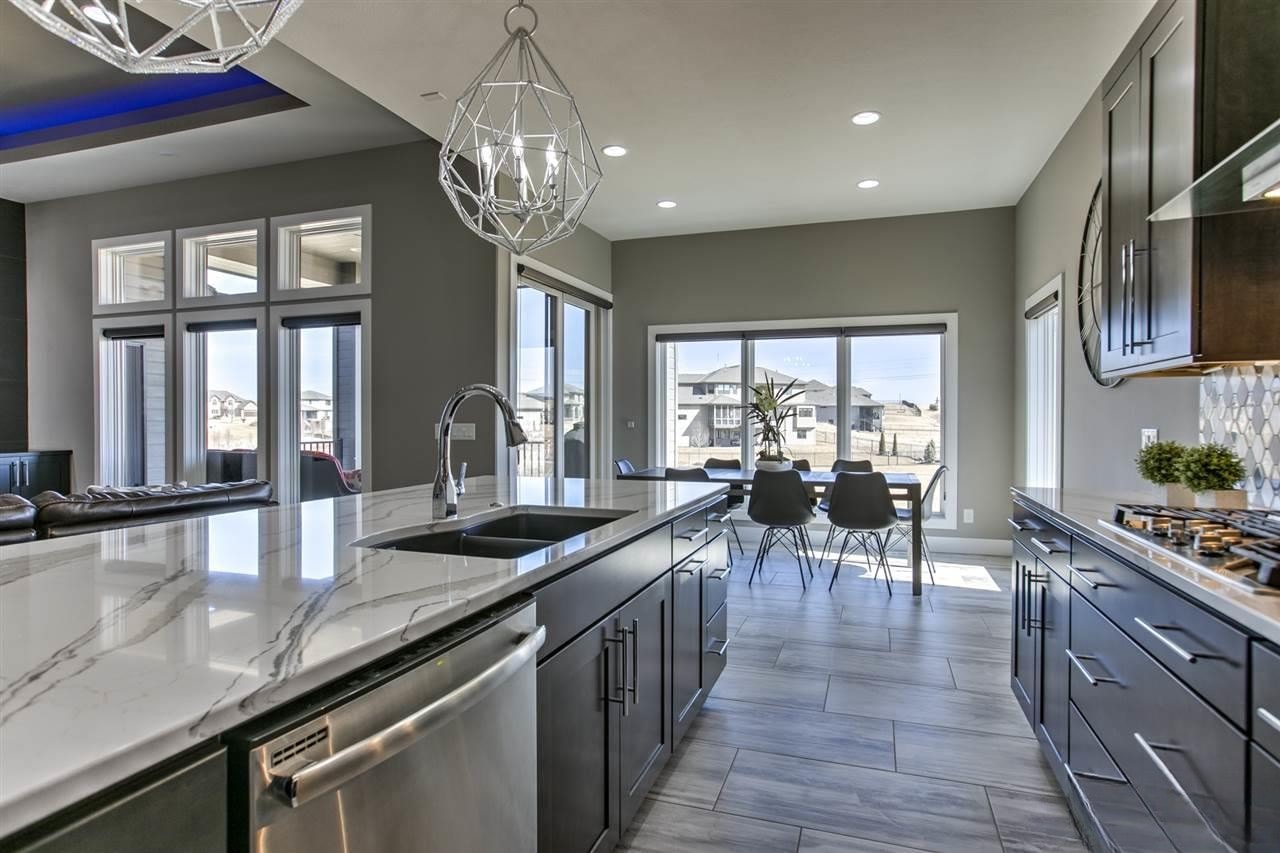 Open concept kitchen with gray cabinetry, marble island, diamond tile backsplash and geometric pendant lights