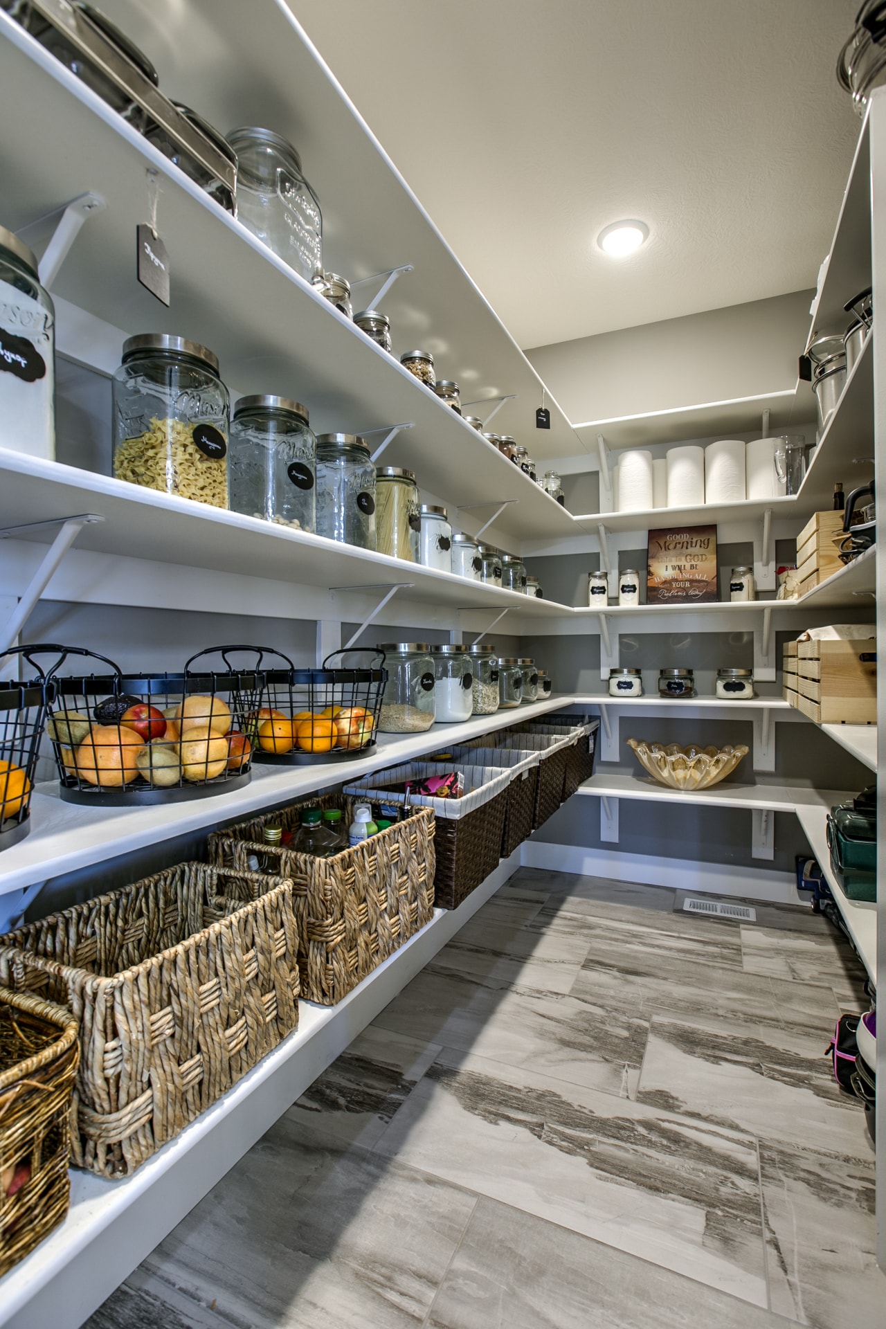 Walk-in pantry with white open shelving, woven baskets, glass jars and large format tile floor