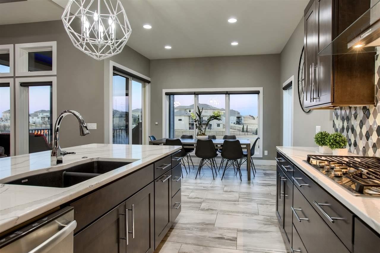Gray kitchen with diamond tile backsplash, marble countertops, farmhouse sink and dining area at dusk