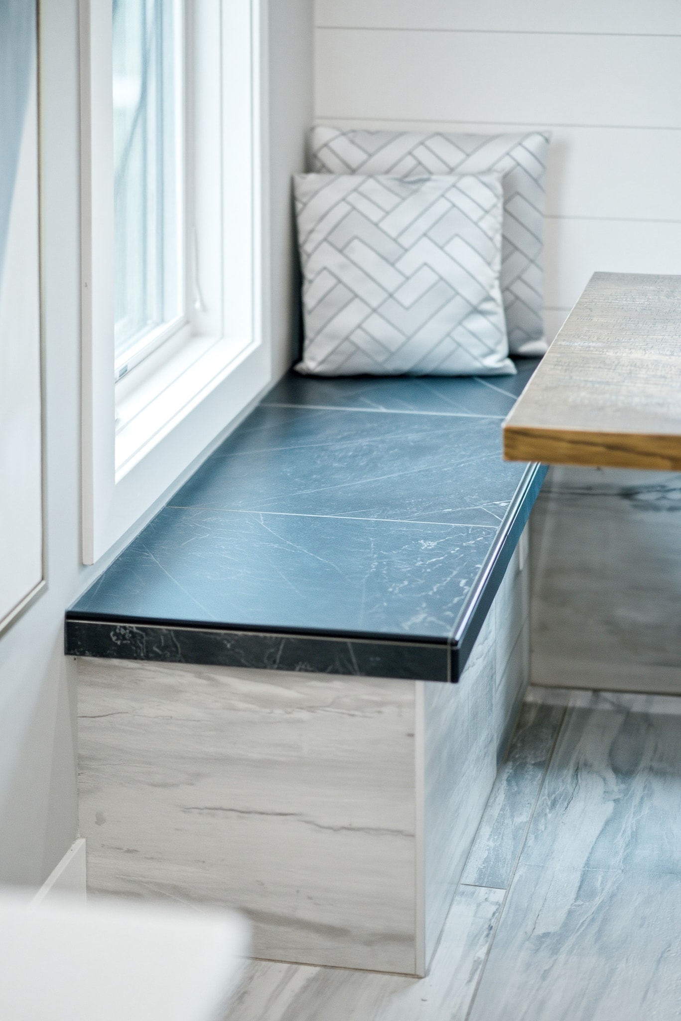 Custom tile window seat bench with dark marble top, wood-look tile surround and herringbone pillow detail