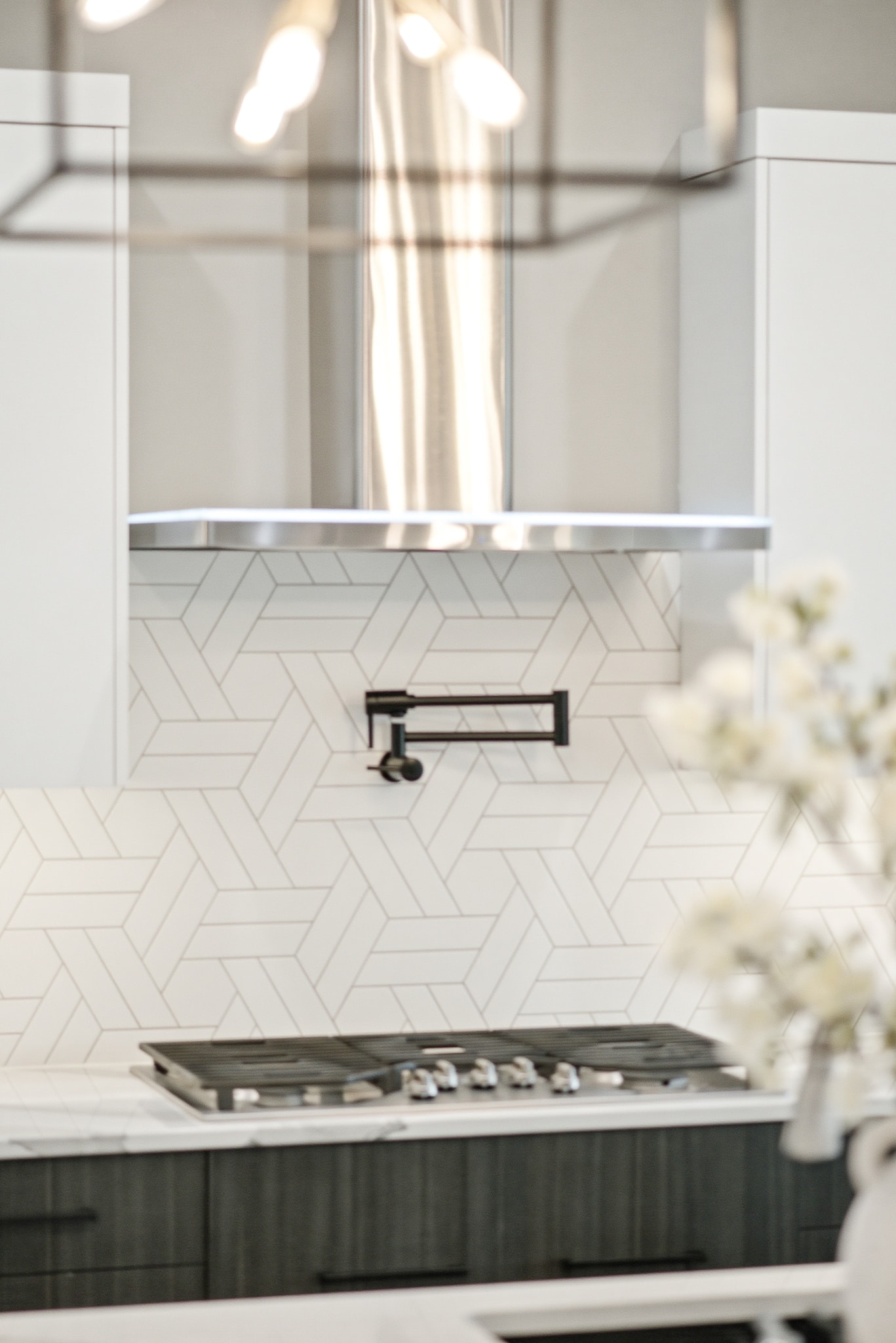 Close-up of white geometric tile backsplash with black pot filler and stainless range hood