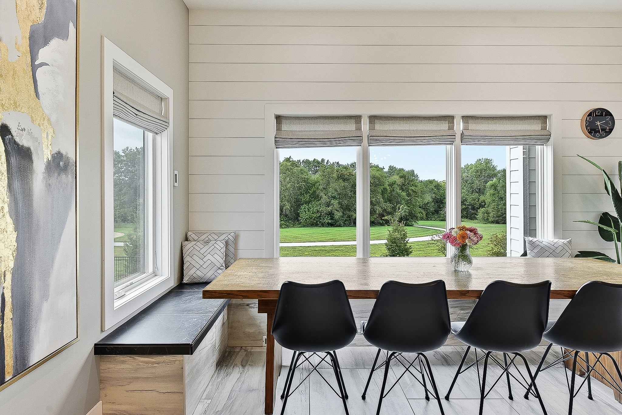 Dining nook with tile bench seat, live-edge wood table, black chairs and large windows overlooking backyard