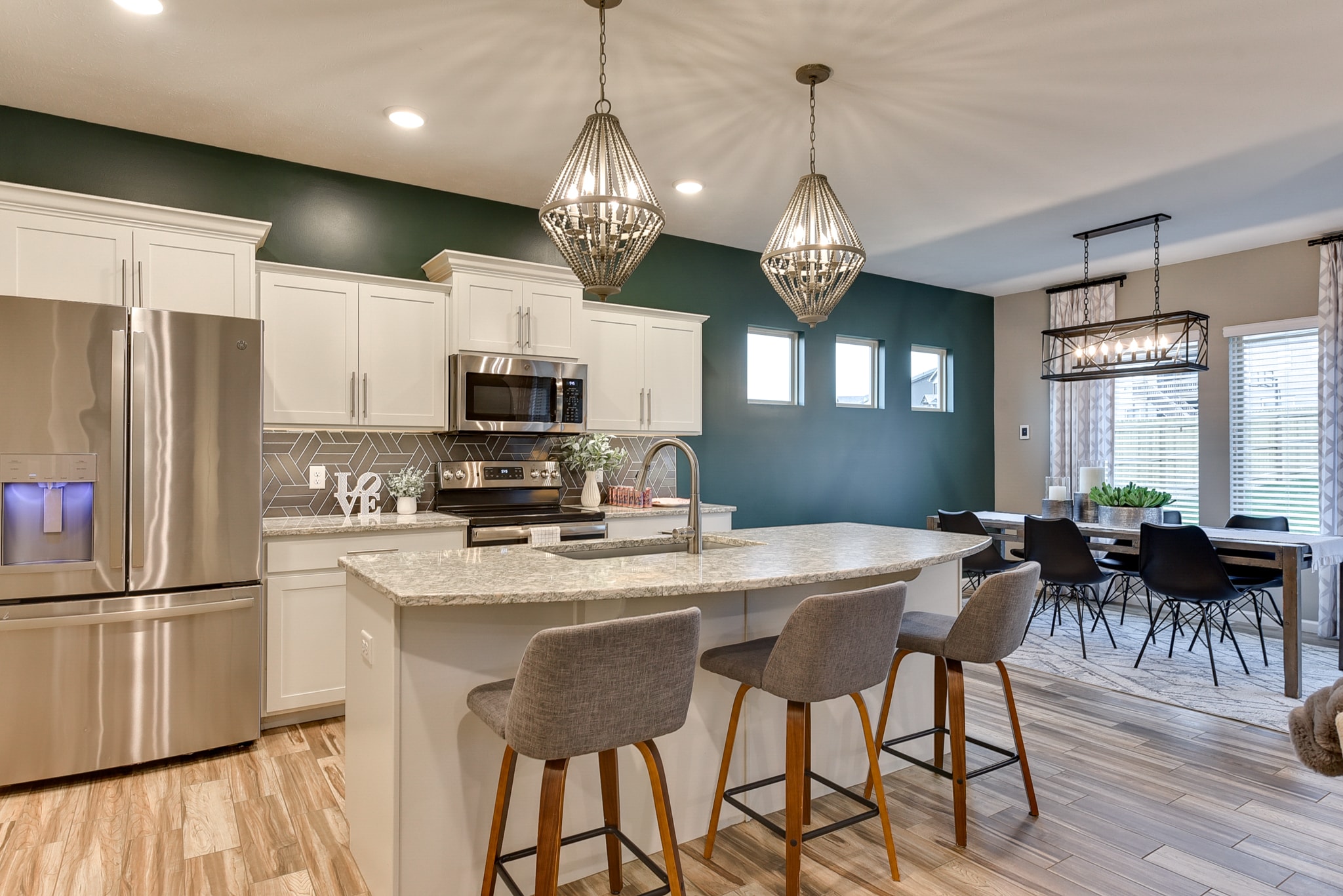 Wide view of kitchen with teal accent wall, white cabinets, geometric tile backsplash, granite island and dining area