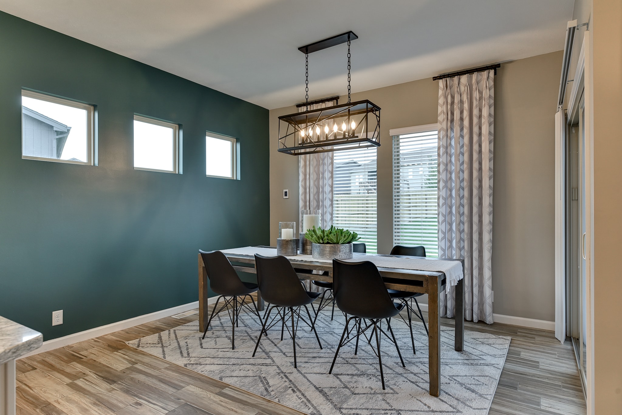 Dining room with teal accent wall, wood farmhouse table, black chairs and rectangular cage chandelier