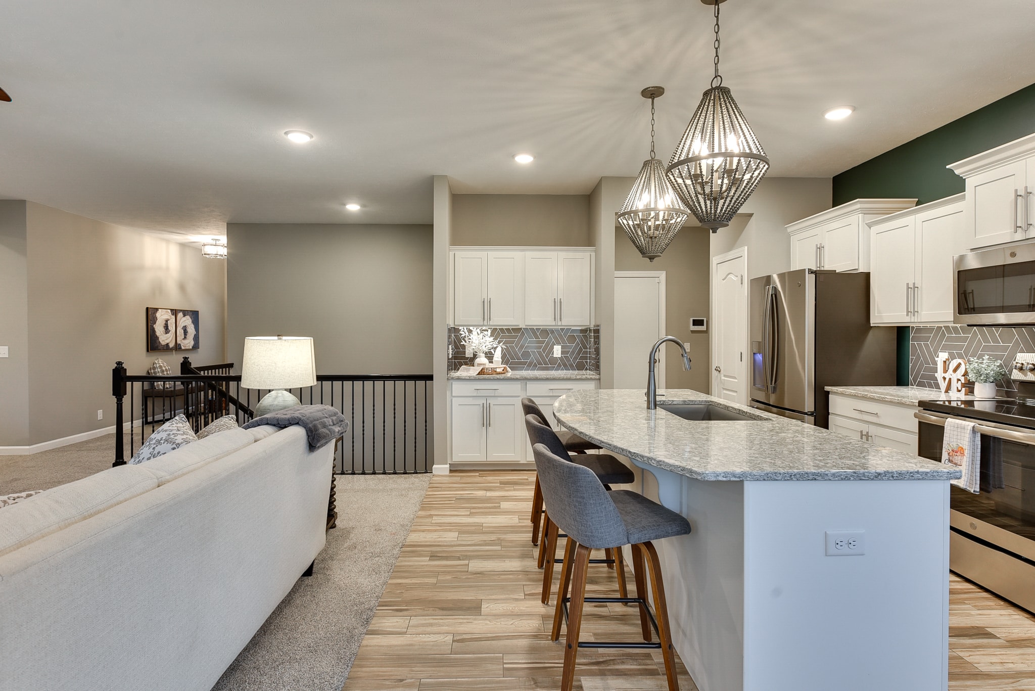 Open concept kitchen and living room with white cabinets, geometric tile backsplash, granite island and bead pendants
