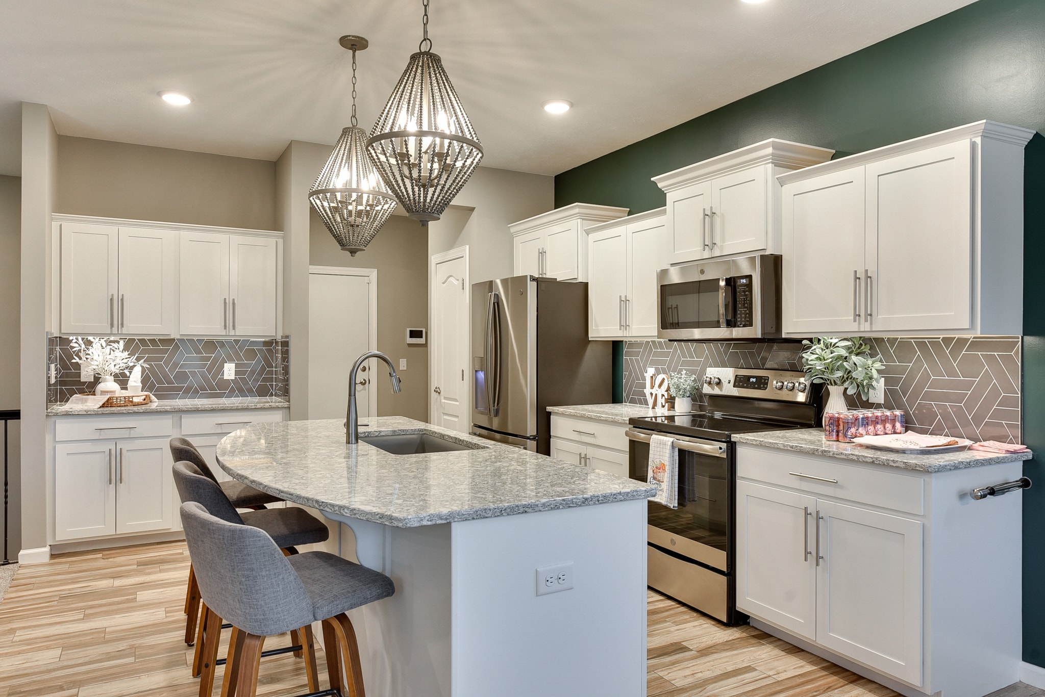 Kitchen with white cabinetry, geometric gray tile backsplash, granite island, bead pendants and teal accent wall