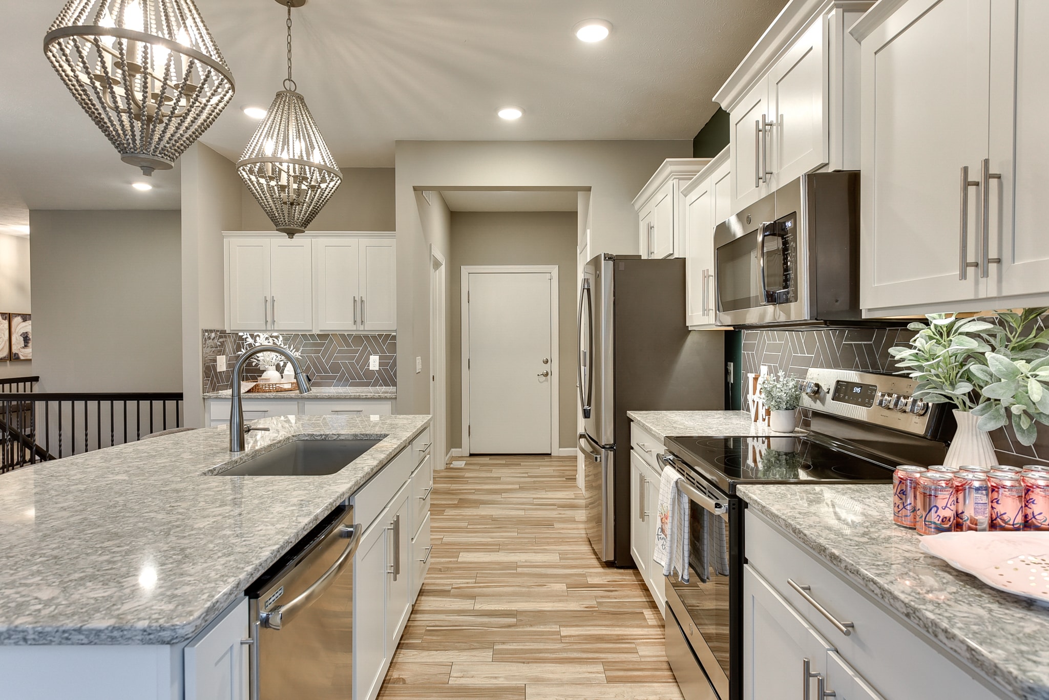 Kitchen with white cabinets, geometric tile backsplash, granite countertops and bead chandelier pendants