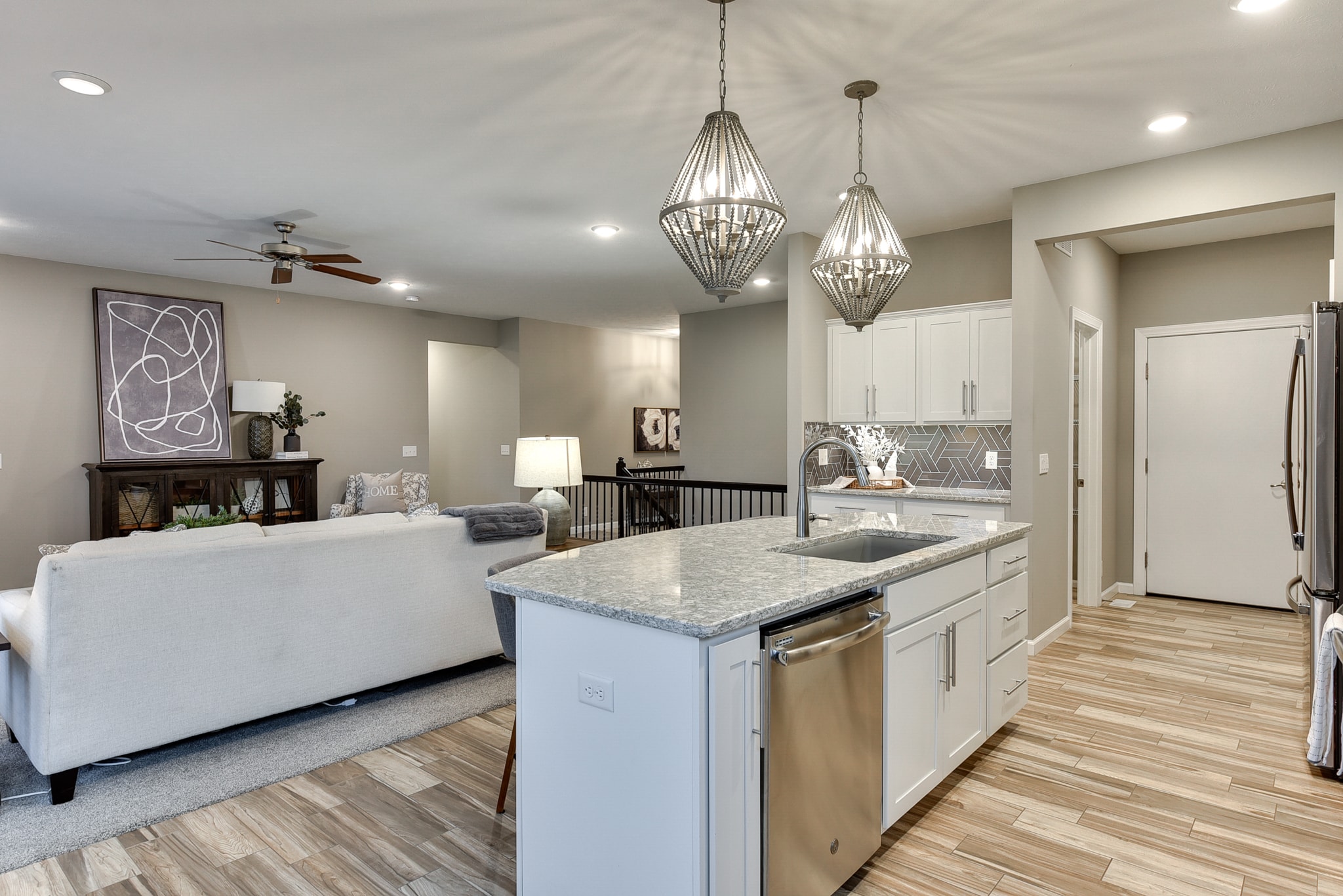Open concept kitchen and living room with white cabinets, geometric tile backsplash, granite island and living area
