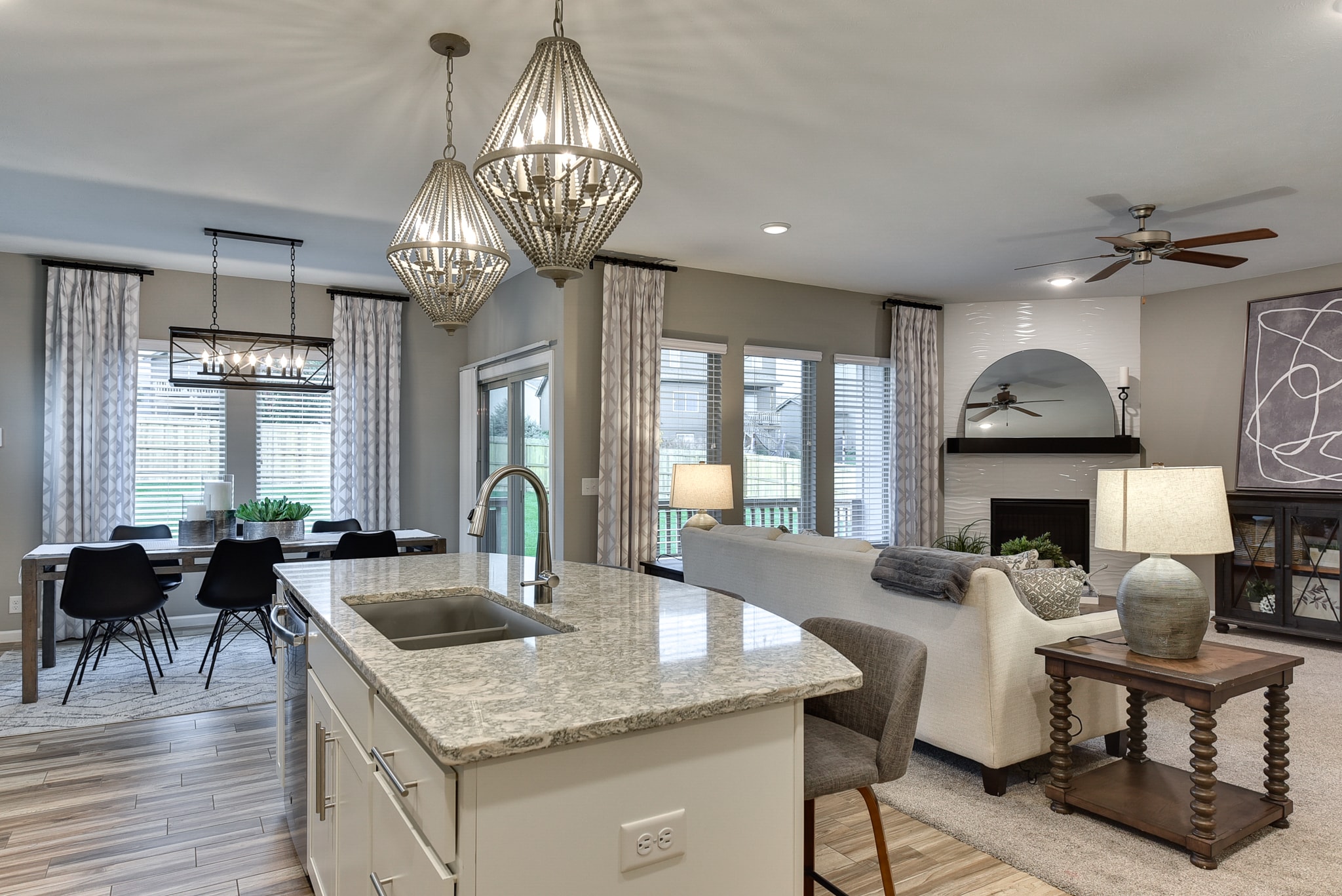 Open concept kitchen with granite island, bead pendants, dining area and fireplace living room beyond