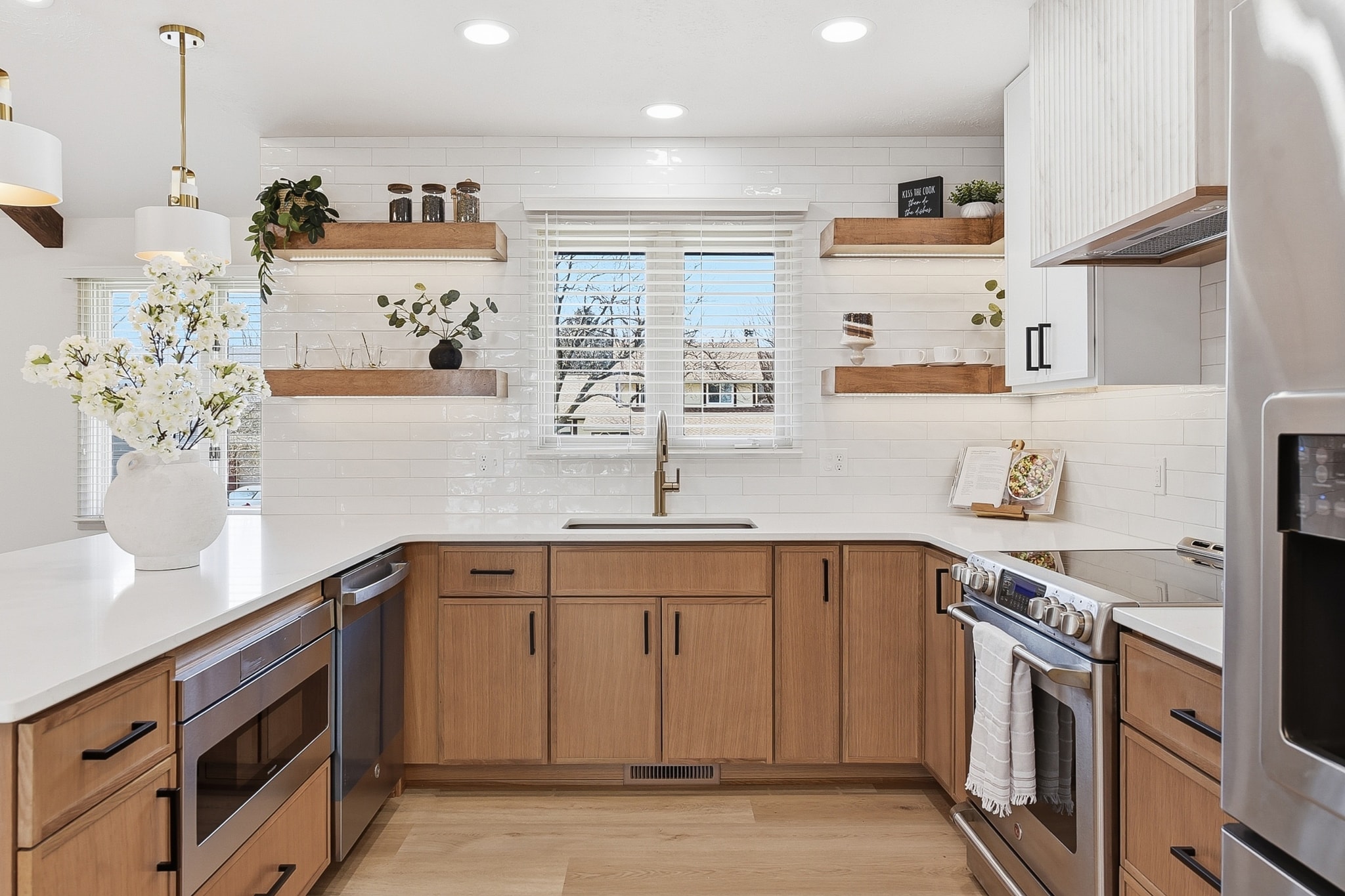 Wide view of farmhouse kitchen with white subway tile, wood lower cabinets, open shelving and gold pendant lights