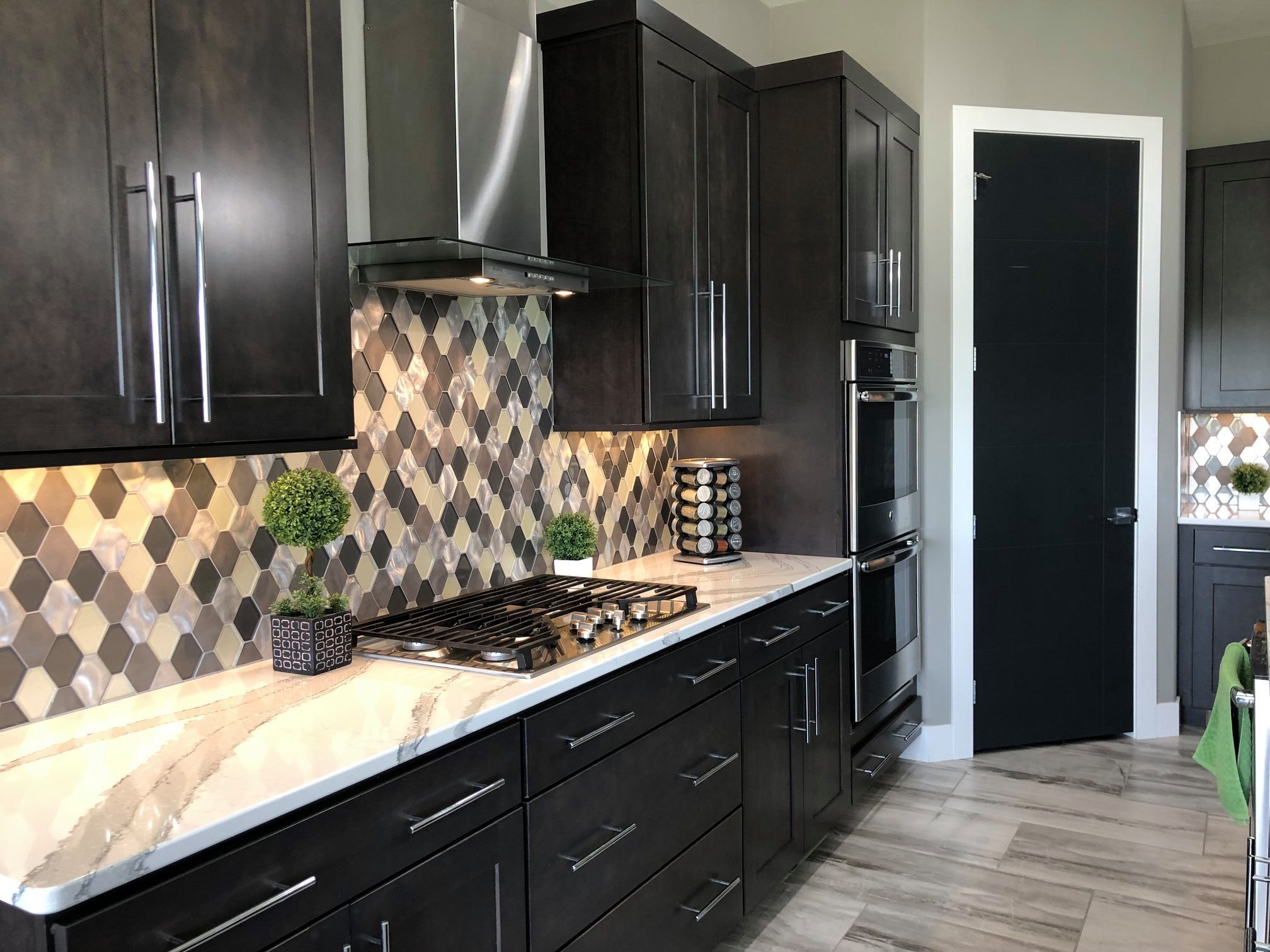 Dark kitchen with metallic diamond tile backsplash, espresso cabinetry, marble countertops and stainless range hood