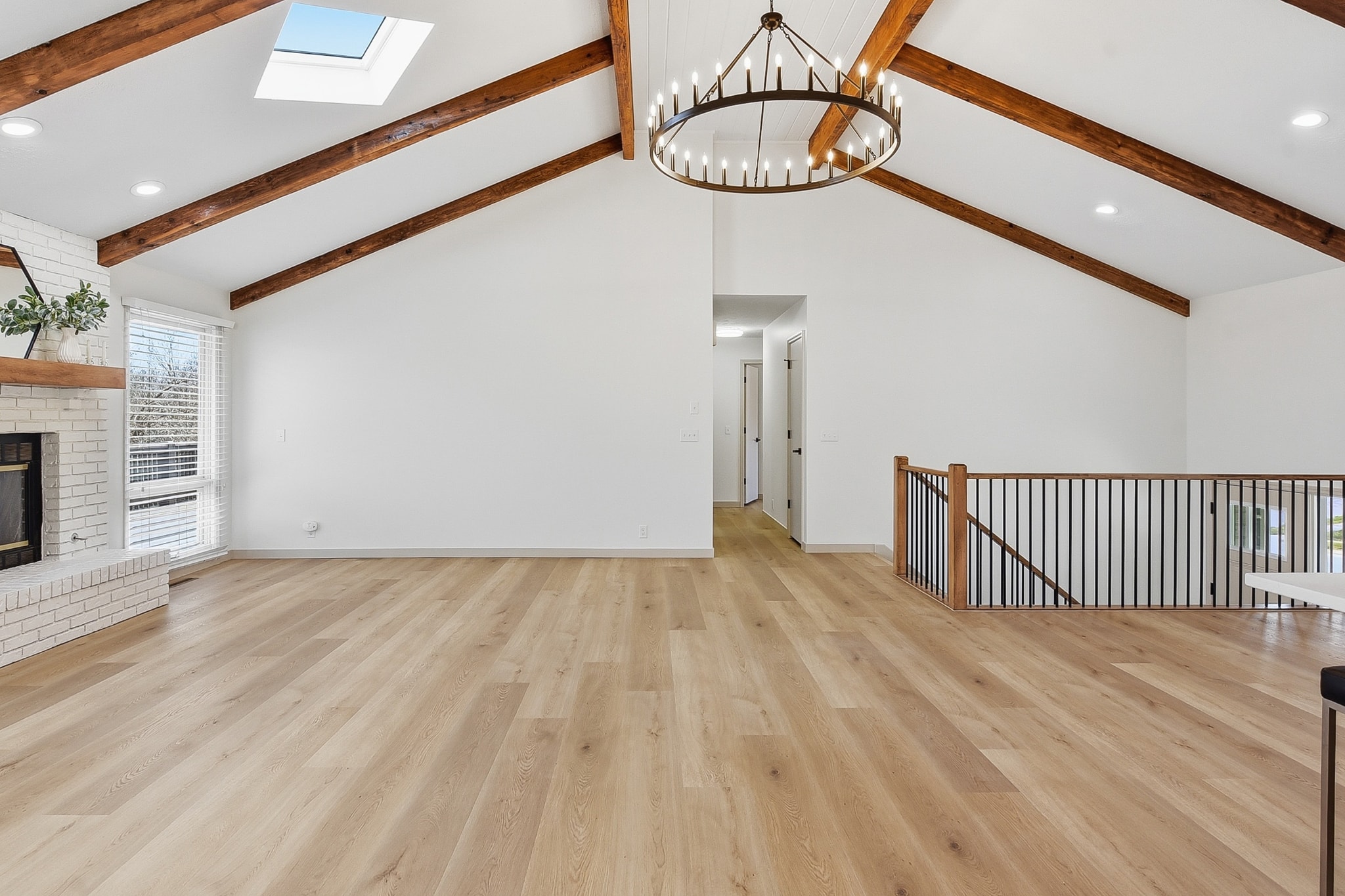 Vaulted living room with LVP flooring, white brick fireplace and chandelier