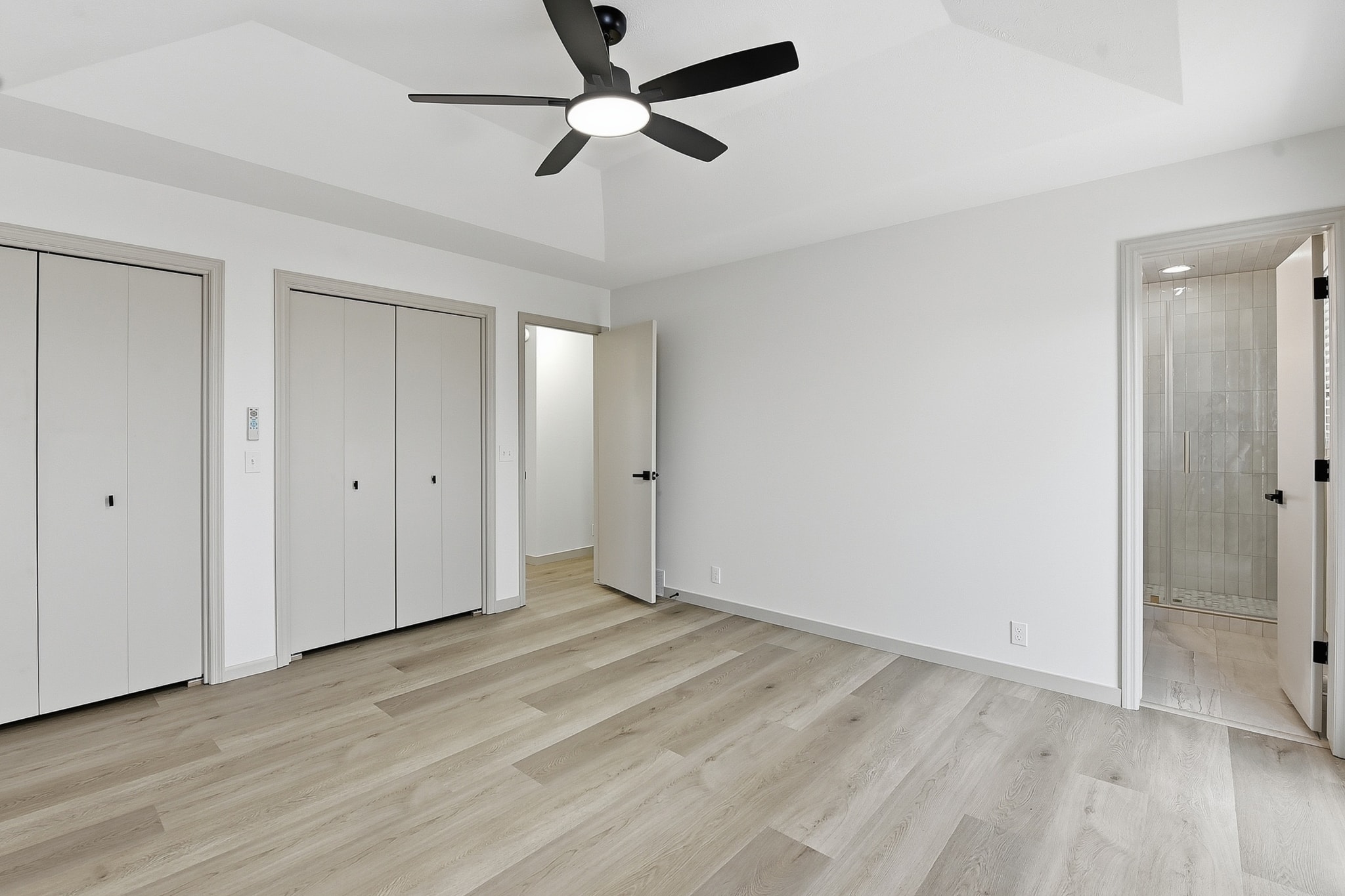 Master bedroom with light oak LVP flooring, ceiling fan and en-suite bathroom
