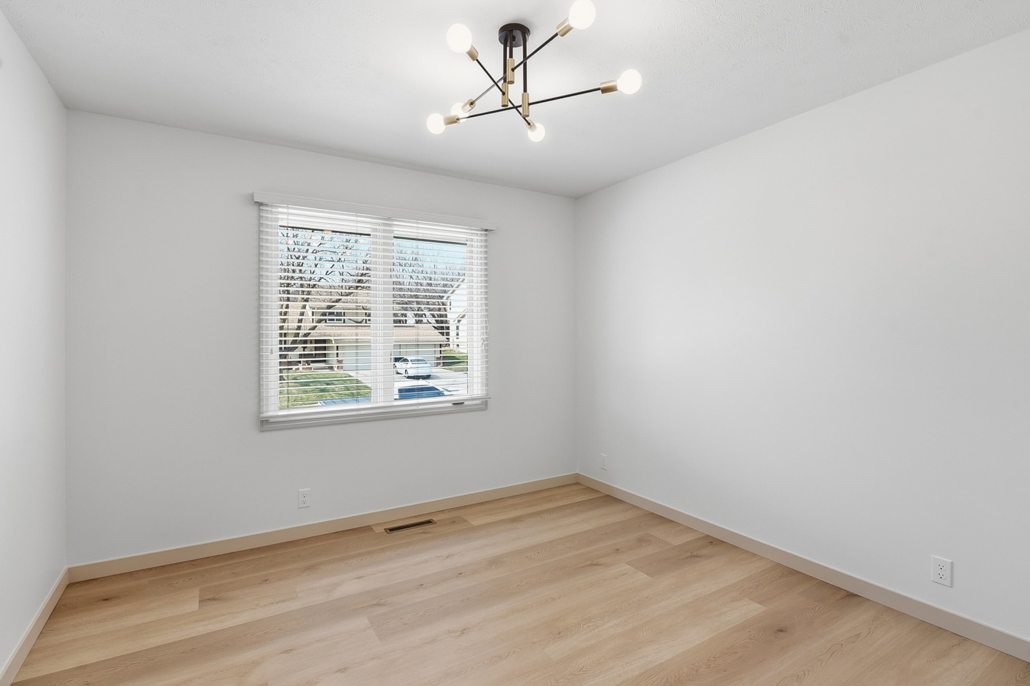 Clean bedroom with light LVP flooring, sputnik chandelier and natural light
