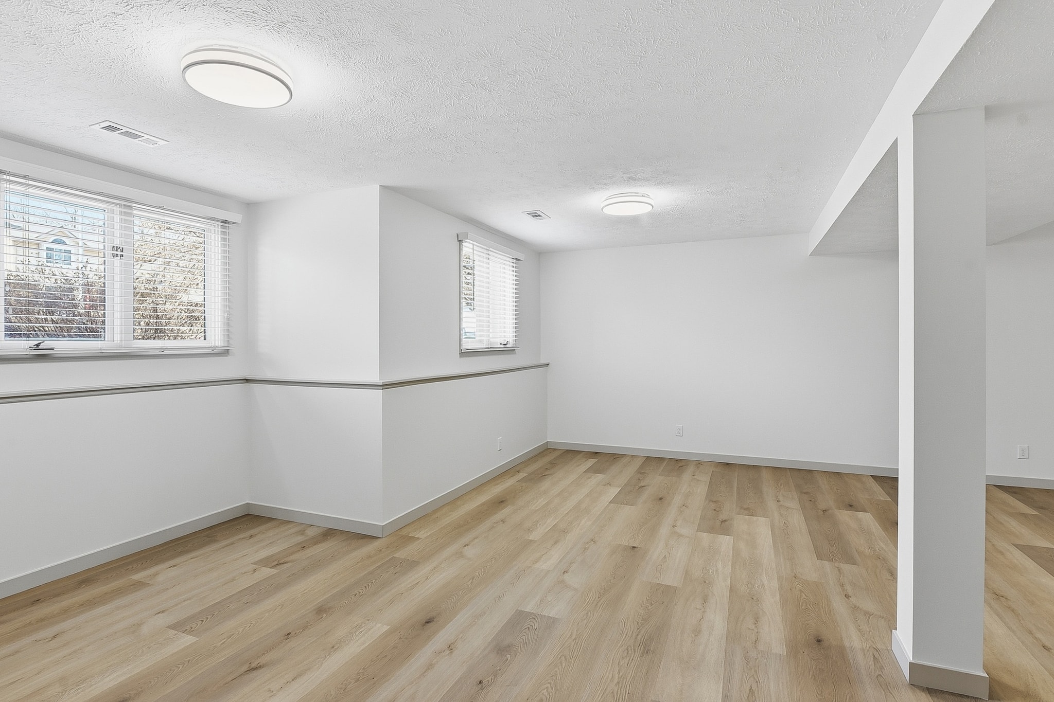 Finished basement with light LVP flooring, white walls and egress windows