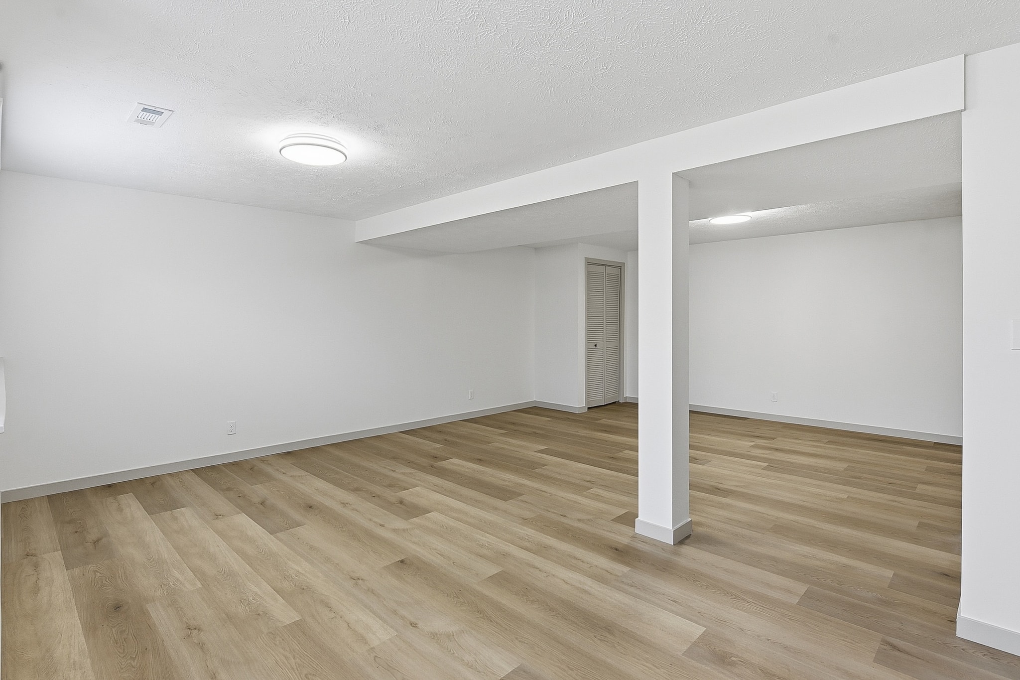 Open basement with medium-tone LVP flooring, support columns and utility lighting