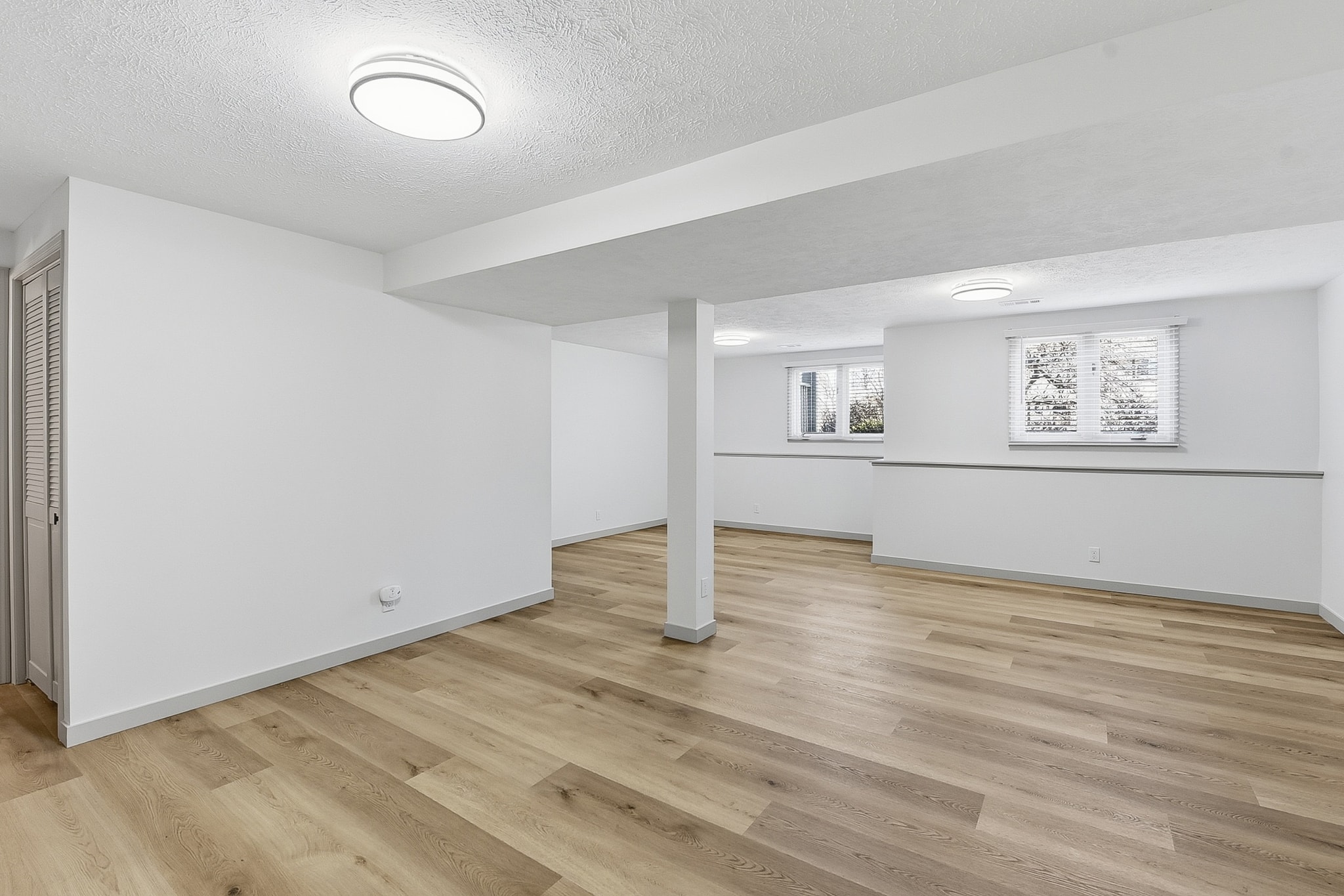 Spacious finished basement with light LVP flooring, columns and egress windows