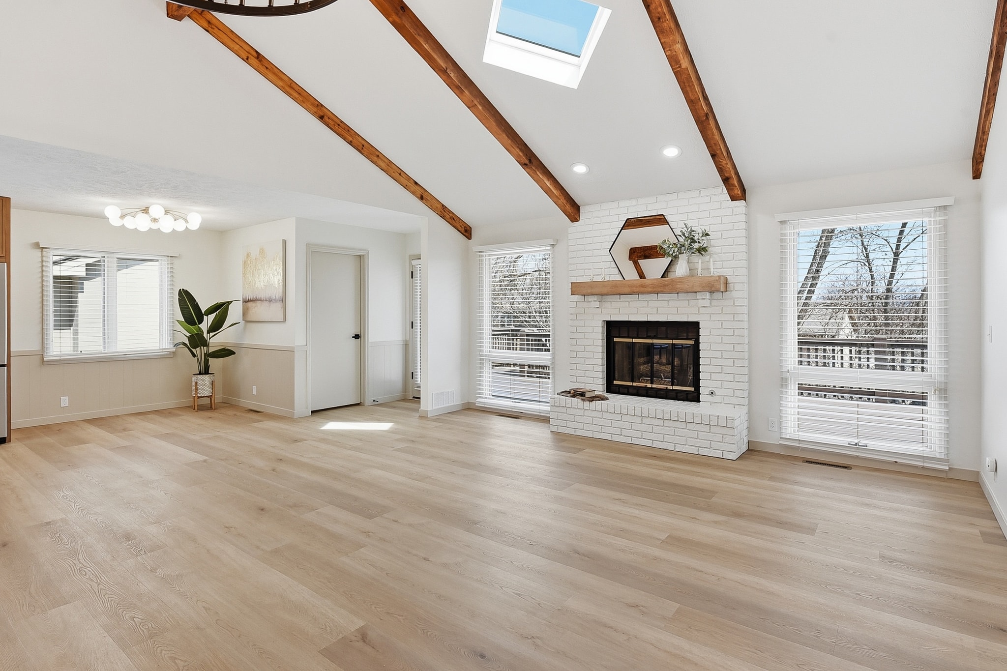 Living room with LVP flooring, white brick fireplace and exposed wood beams