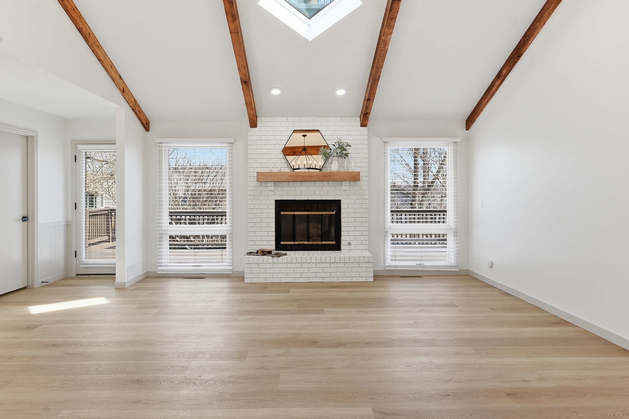 Bright living room with LVP flooring, white brick fireplace and skylight