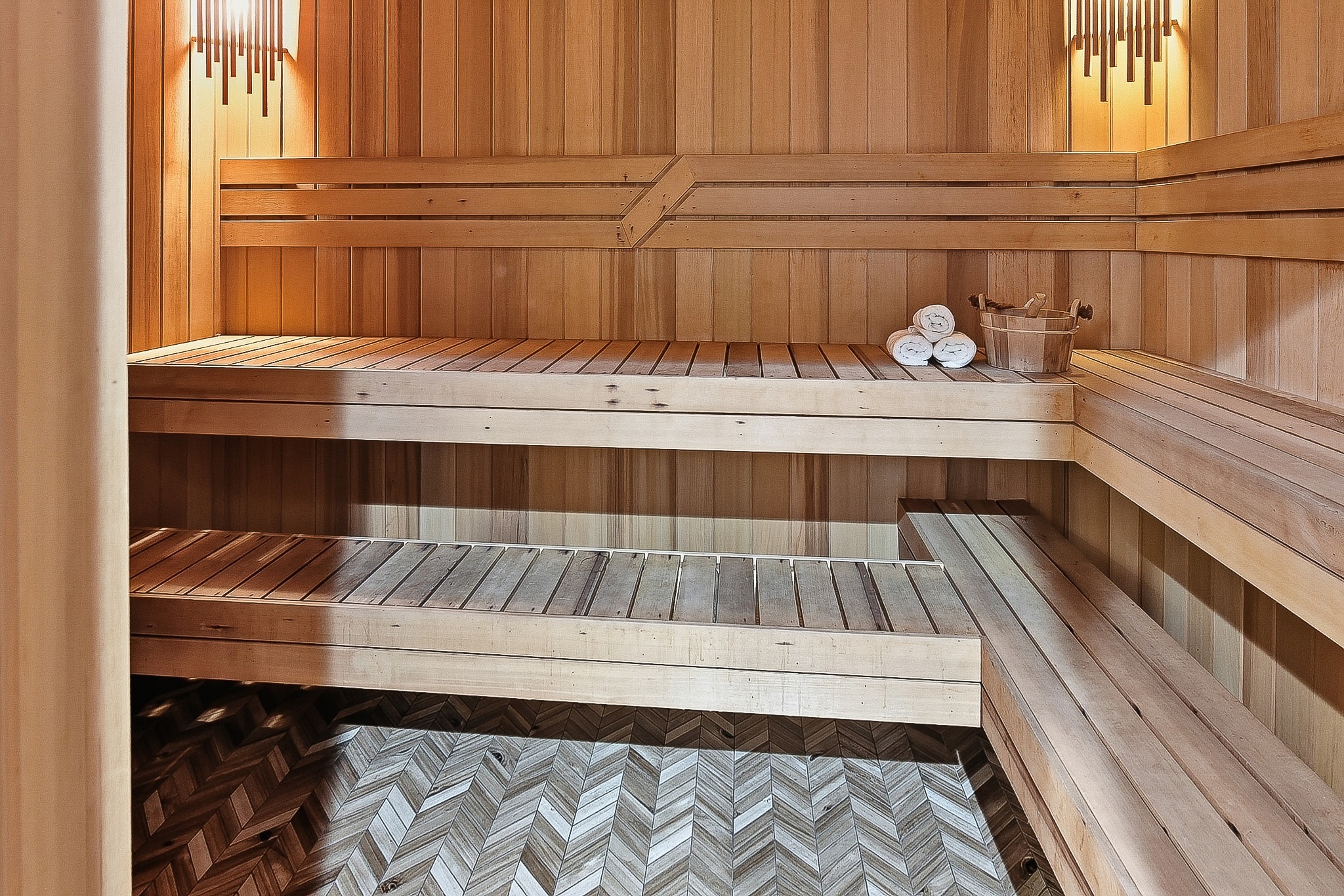 Multi-level cedar sauna benches with herringbone tile floor and warm pendant lighting