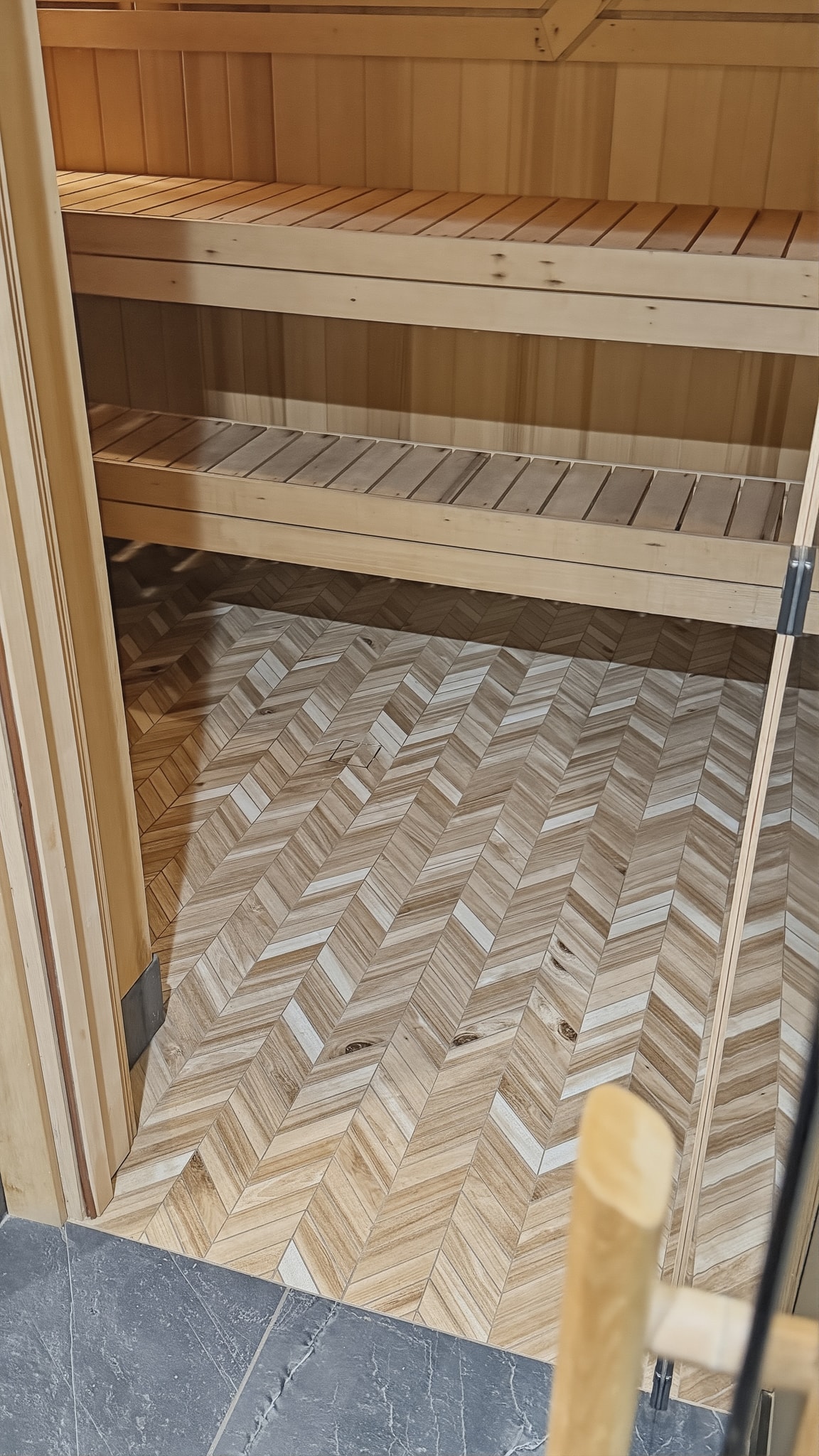 Close-up of custom herringbone tile floor inside cedar sauna with glass door