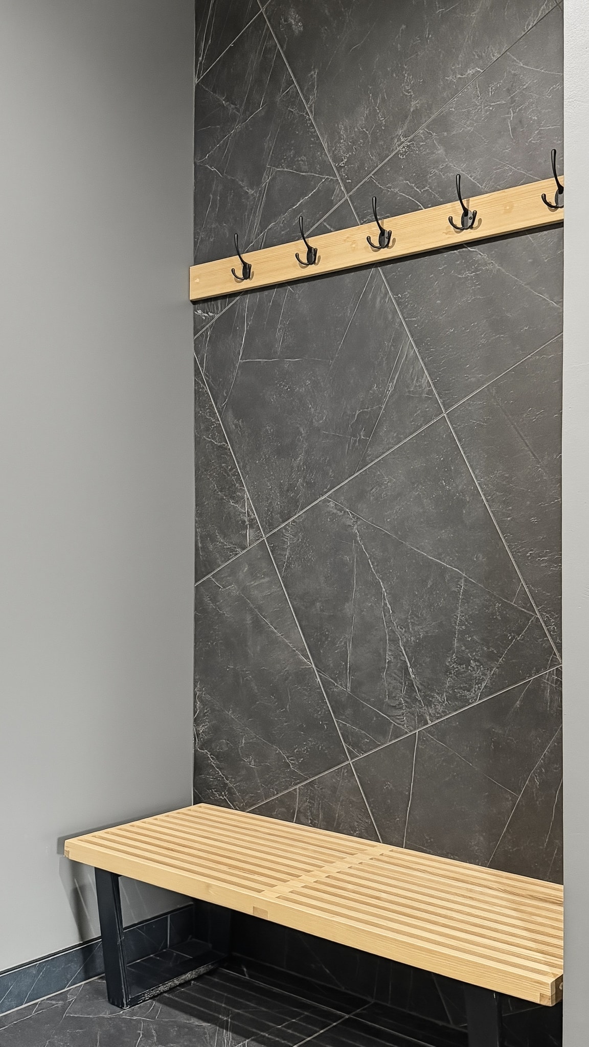 Dark marble tile accent wall with wood bench and black coat hooks in sauna changing area